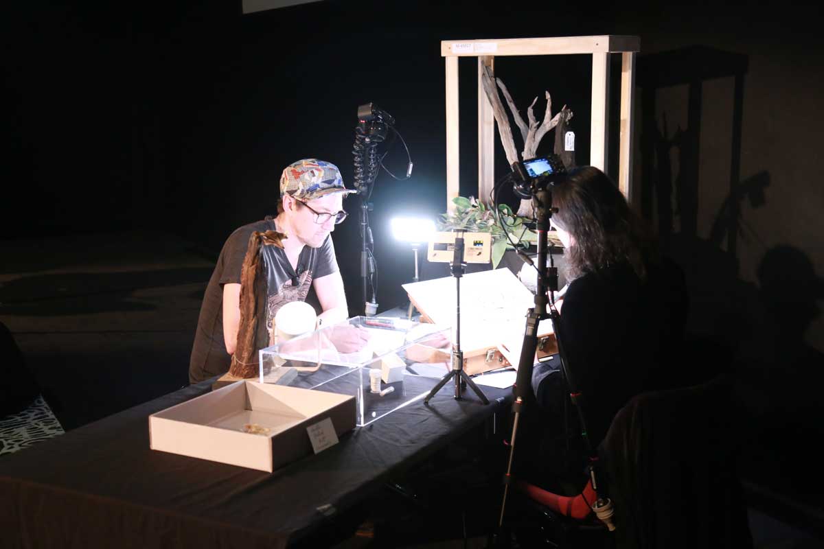 A man and a woman sit at a table with bat specimens, drawing